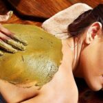 Eine Frau erhält in einem Spa eine Behandlung mit einer grünen Kräutermaske für den Rücken.