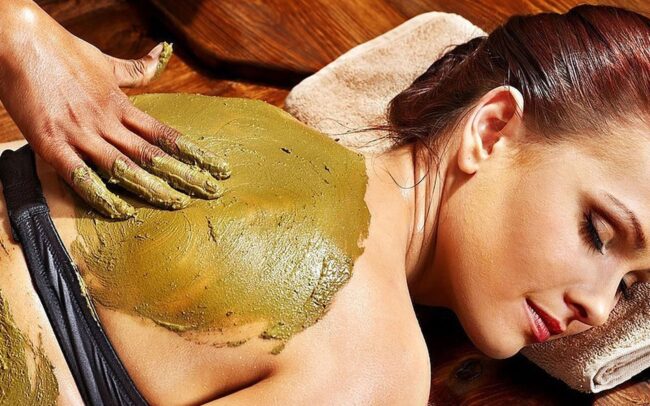Eine Frau erhält in einem Spa eine Behandlung mit einer grünen Kräutermaske für den Rücken.