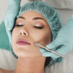 Eine Frau genießt eine Wellness-Gesichtsbehandlung mit einem Skalpell durch einen Fachmann, der Handschuhe und eine Haarmütze trägt, im Spa.