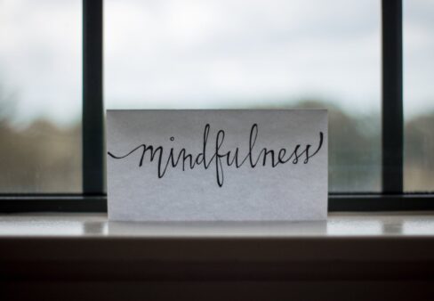 Eine weiße Karte mit dem kursiv geschriebenen Wort Achtsamkeit, die auf einer Fensterbank liegt.