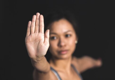 Eine Frau streckt ihren Arm mit geöffneter Handfläche nach vorne, als wolle sie Halt signalisieren, vor einem schwarzen Hintergrund.