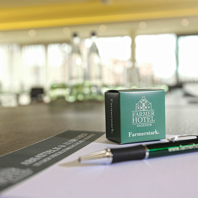 Ein Stift, ein Notizblock und eine Markenbox auf einem Konferenztisch im Farmer Hotel, mit unscharfem Hintergrund.