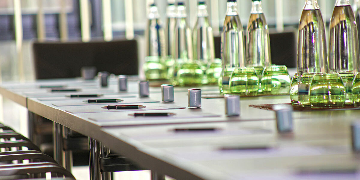 Ein mit Wasserflaschen, Notizblöcken und Stiften gedeckter Konferenztisch in einem modernen Besprechungsraum.