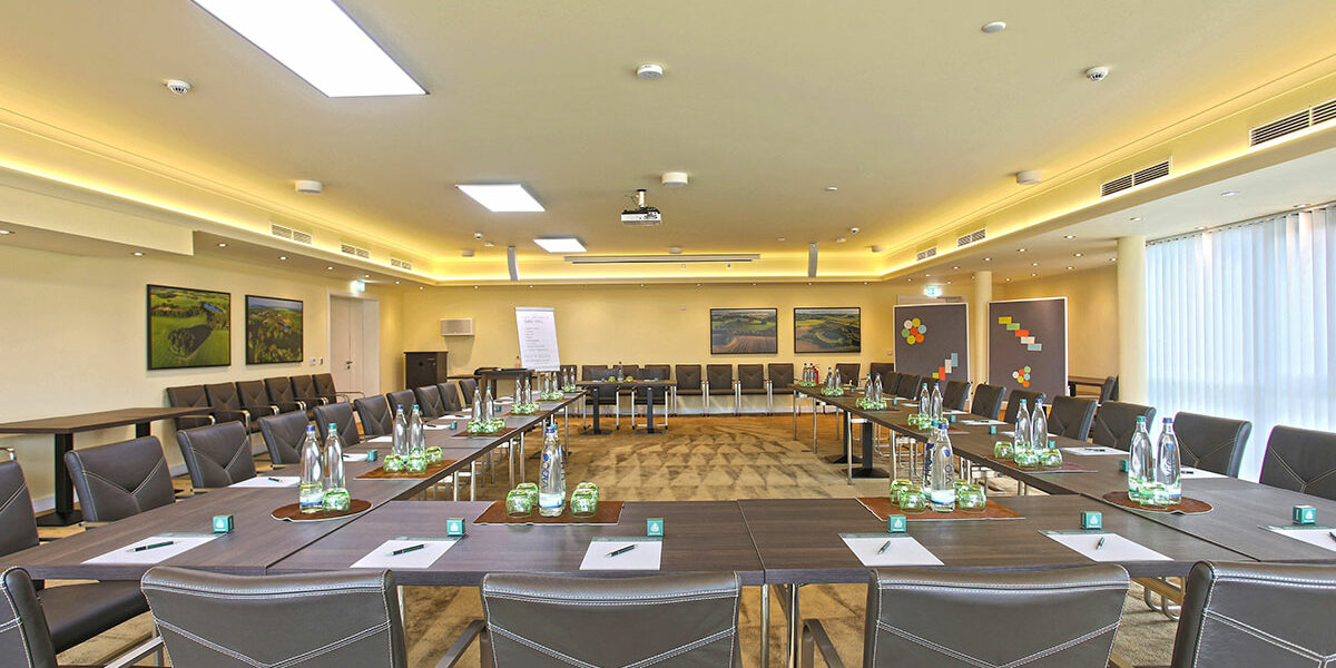 Ein moderner Konferenzraum mit einem U-förmigen Tisch, Stühlen, Wasserflaschen, Notizblöcken und Wandkunst.