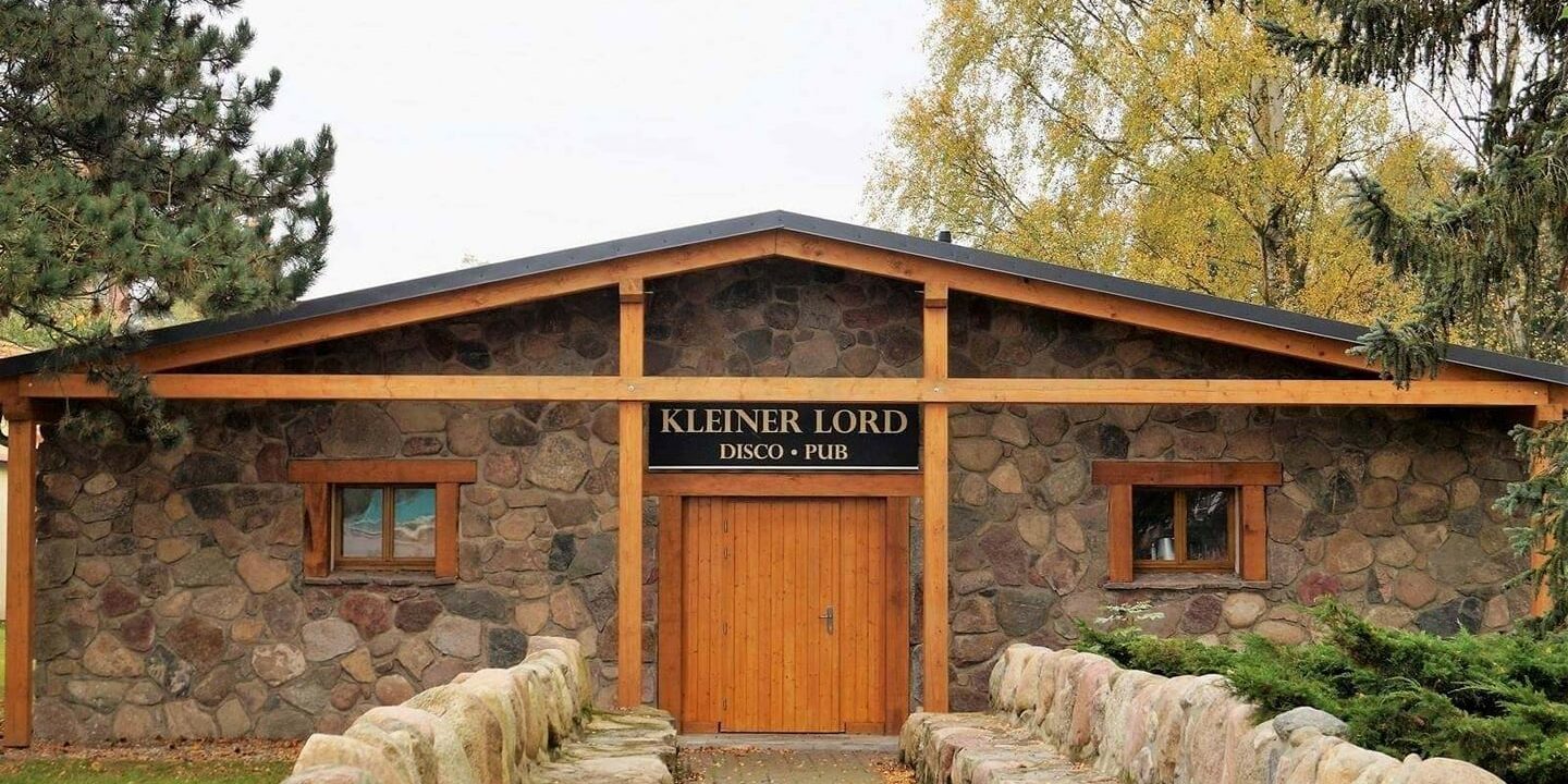 Das charmante Steingebäude mit Holzverkleidung, das als Kleiner Lord Disco Pub bezeichnet wird, steht entlang eines von Bäumen beschatteten Steinwegs.