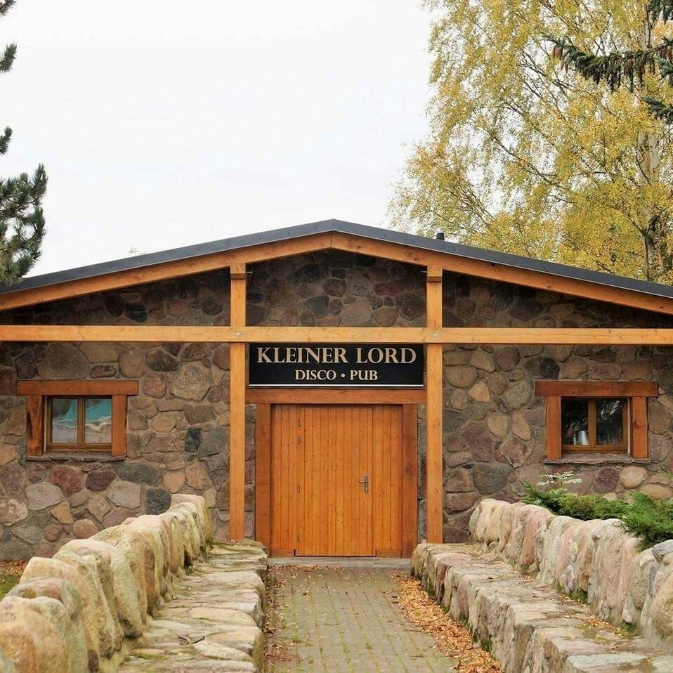 Das charmante Steingebäude mit Holzverkleidung, das als Kleiner Lord Disco Pub bezeichnet wird, steht entlang eines von Bäumen beschatteten Steinwegs.