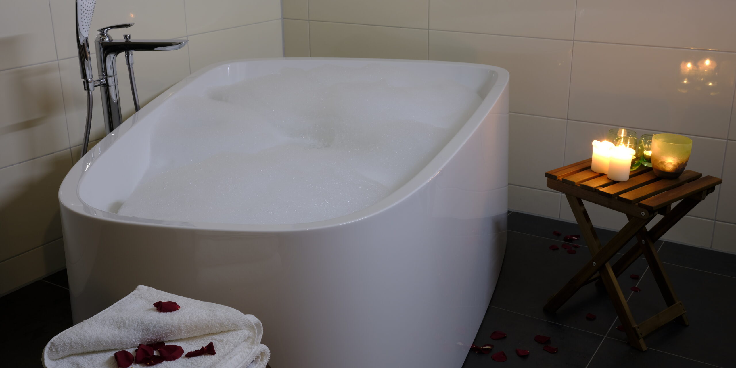 Eine mit Seifenblasen gefüllte Badewanne mit Kerzen, Rosenblättern und gefalteten Handtüchern schafft einen gemütlichen Rückzugsort - perfekt, um sich nach einem produktiven Tag mit der Farmer Suite für ein reibungsloses Farmmanagement zu entspannen.