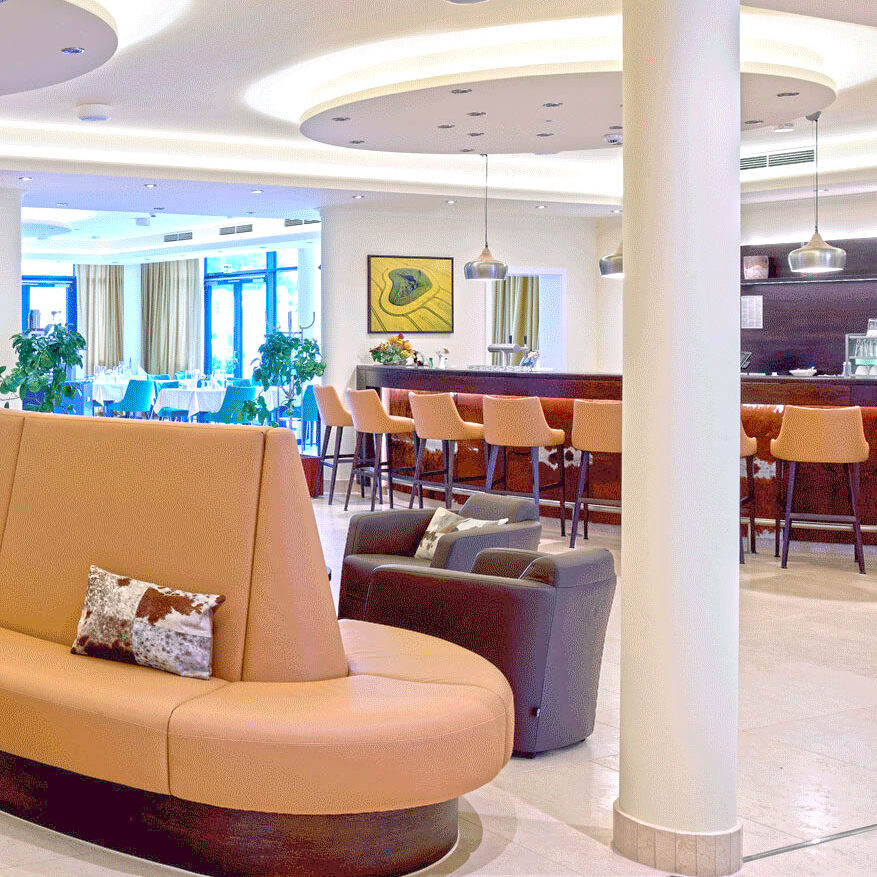 Moderne Hotellobby mit braunen, geschwungenen Sitzmöbeln, Barhockern, Pflanzen und zeitgenössischer Beleuchtung, mit einem stilvollen Bereich für Gastinformationen.
