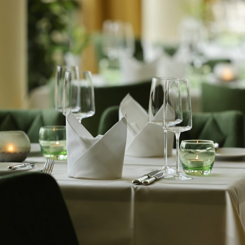 Ein eleganter Restauranttisch mit weißen Servietten, Gläsern, grünen Kerzenhaltern und weißen Tischtüchern schafft einen raffinierten Essbereich.