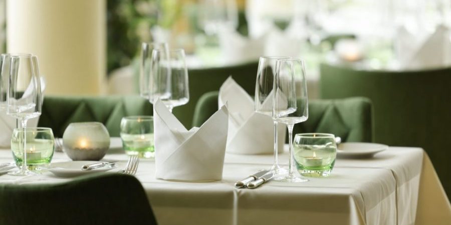Eleganter Restauranttisch in einem stilvollen Bereich, gedeckt mit gefalteten Servietten, Weingläsern, grünen Wassergläsern und Kerzen. Eleganter Restauranttisch in einem stilvollen Bereich, gedeckt mit gefalteten Servietten, Weingläsern, grünen Wassergläsern und Kerzen.