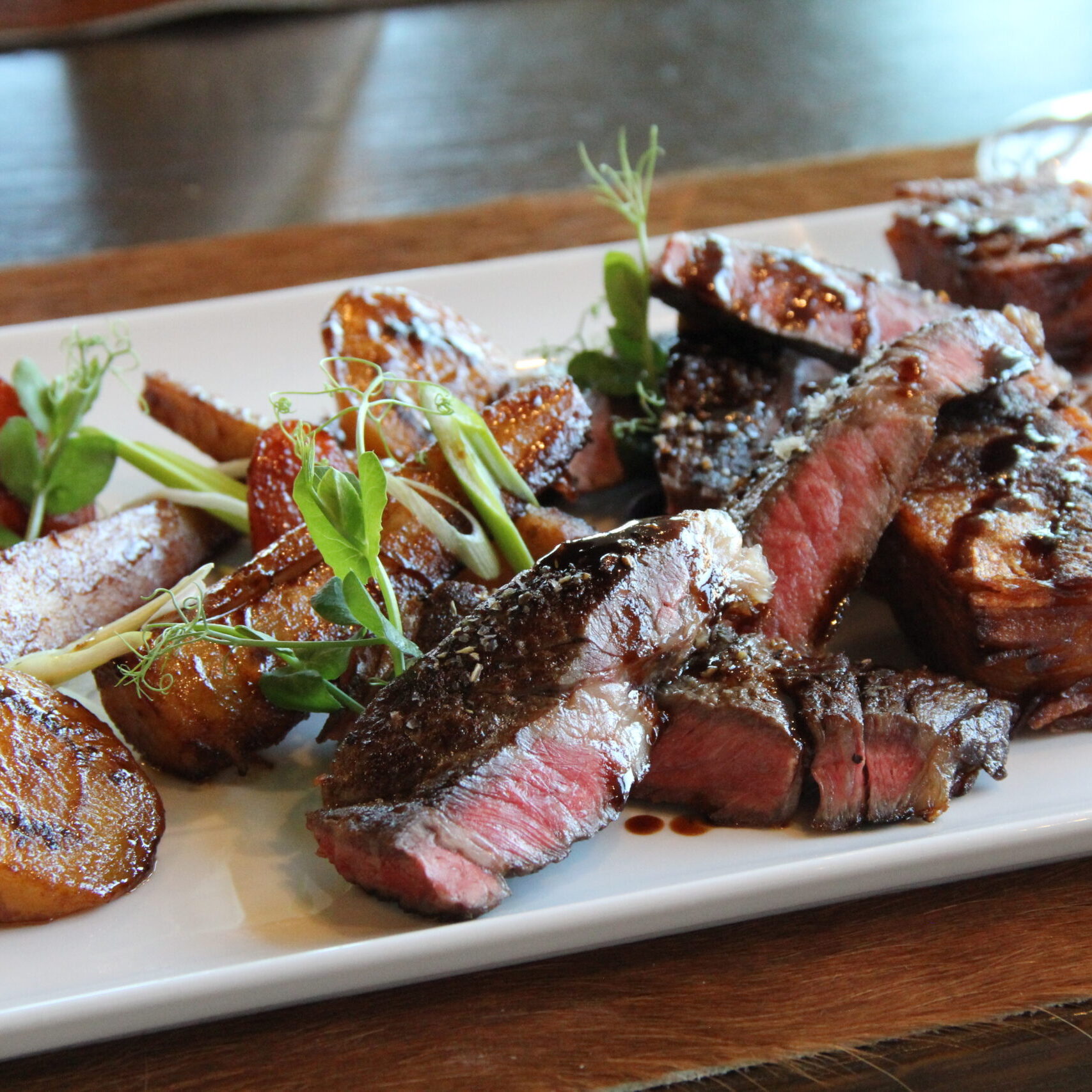 Geschnittenes Steak mit Bratkartoffeln und frischen Kräutern, fachmännisch zubereitet von unserem Koch (m/w/d), serviert auf einem weißen rechteckigen Teller.