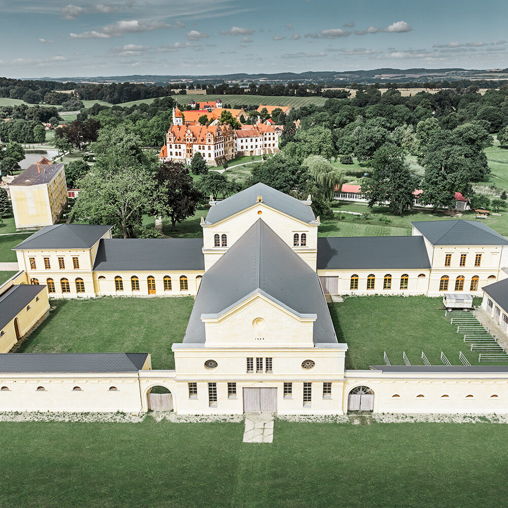 Luftaufnahme eines großen, gelben historischen Gebäudekomplexes, bekannt als „Marstall“, umgeben von grünen Rasenflächen und Bäumen.