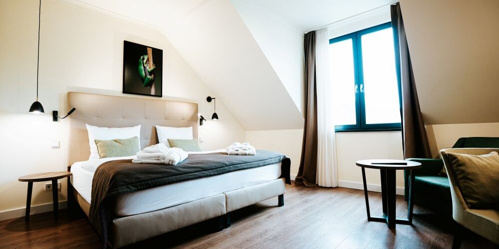 Modernes Doppelzimmer mit Komfort: Doppelbett, Holzfußboden, gemütliche Sitzecke und großes Fenster mit Vorhängen.