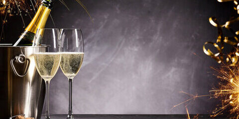 Champagnerflasche im Eiskübel, zwei gefüllte Gläser, Wunderkerzen und festliche Dekorationen auf dunklem Hintergrund - perfekt für einen stilvollen Jahresausklang oder eine prickelnde Feier zu Silvester 2026.