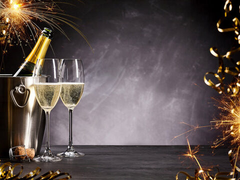 Champagnerflasche im Eiskübel, zwei gefüllte Gläser, Wunderkerzen und festliche Dekorationen auf dunklem Hintergrund - perfekt für einen stilvollen Jahresausklang oder eine prickelnde Feier zu Silvester 2026.