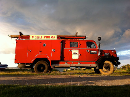 Ein leuchtend roter Truck mit der Aufschrift WanderKino Mobile Cinema steht unter freiem Himmel und lädt Kinofreunde mit einem Ticket "WanderKino 2026" zu einem unvergesslichen Filmerlebnis ein.