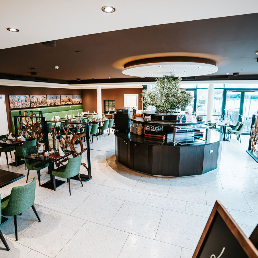 Modernes Restaurantinterieur mit grünen Stühlen, Holztischen und großen Fenstern, die natürliches Licht hereinlassen.