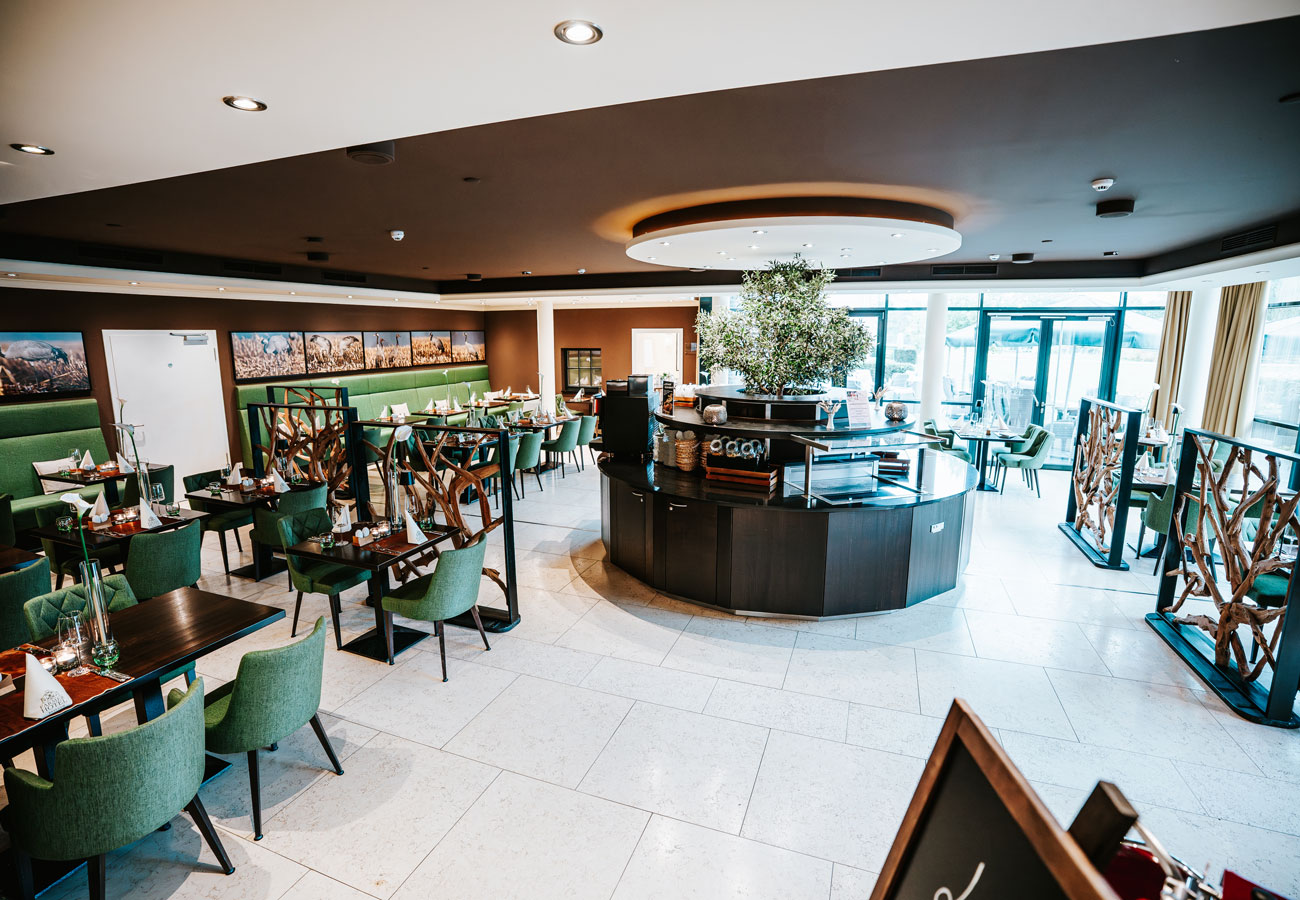 Modernes Restaurantinterieur mit grünen Stühlen, Holztischen und großen Fenstern, die natürliches Licht hereinlassen.