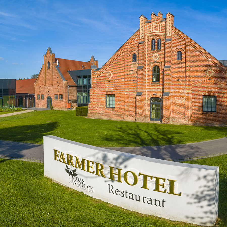 Rotes Backsteingebäude mit FARMER HOTEL Restaurantschild auf grünem Rasen unter blauem Himmel.