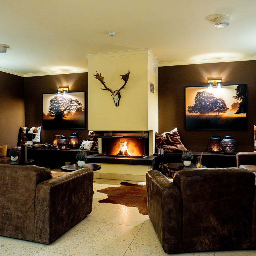 Gemütliches Wohnzimmer mit braunen Sofas, Kamin, Wandkunst und Hirschgeweih über dem Kaminsims.