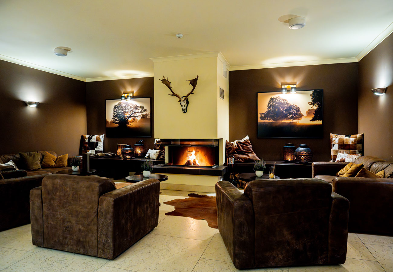 Gemütliches Wohnzimmer mit braunen Sofas, Kamin, Wandkunst und Hirschgeweih über dem Kaminsims.