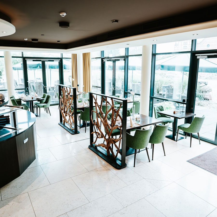 Modernes Café-Interieur mit grünen Stühlen, großen Fenstern, natürlichem Licht und dekorativen Holztrennwänden.