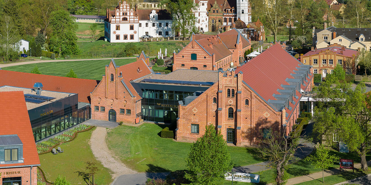 Luftaufnahme von roten Backsteingebäuden und historischen Strukturen inmitten von Grünanlagen an einem sonnigen Tag.