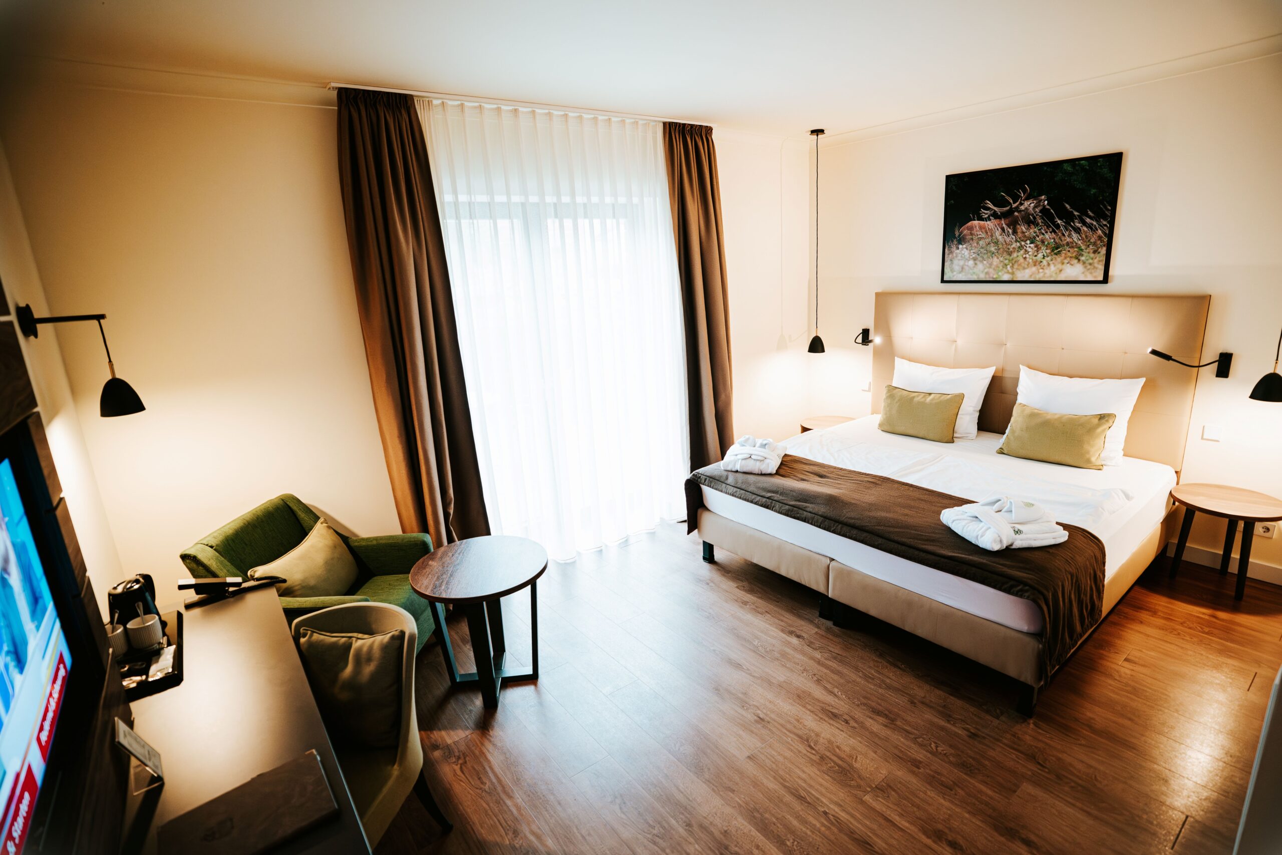 Modernes Hotelzimmer mit einem Doppelbett, einem Sessel, einem Schreibtisch und einem großen Fenster mit transparenten Vorhängen. Modernes Hotelzimmer mit einem Doppelbett, einem Sessel, einem Schreibtisch und einem großen Fenster mit transparenten Vorhängen.
